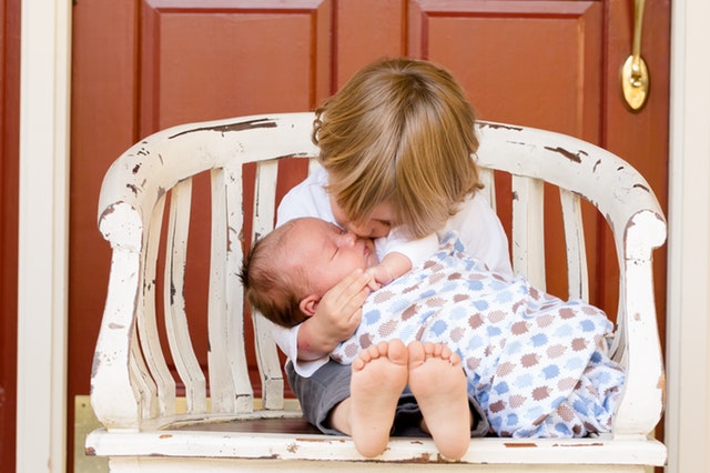 big brother holds baby brother while sitting on a bench